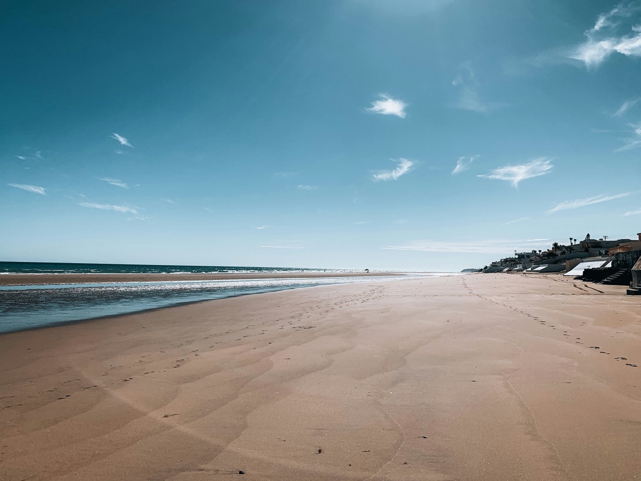 Wide empty beach at low tide with beachfront homes, sunny day